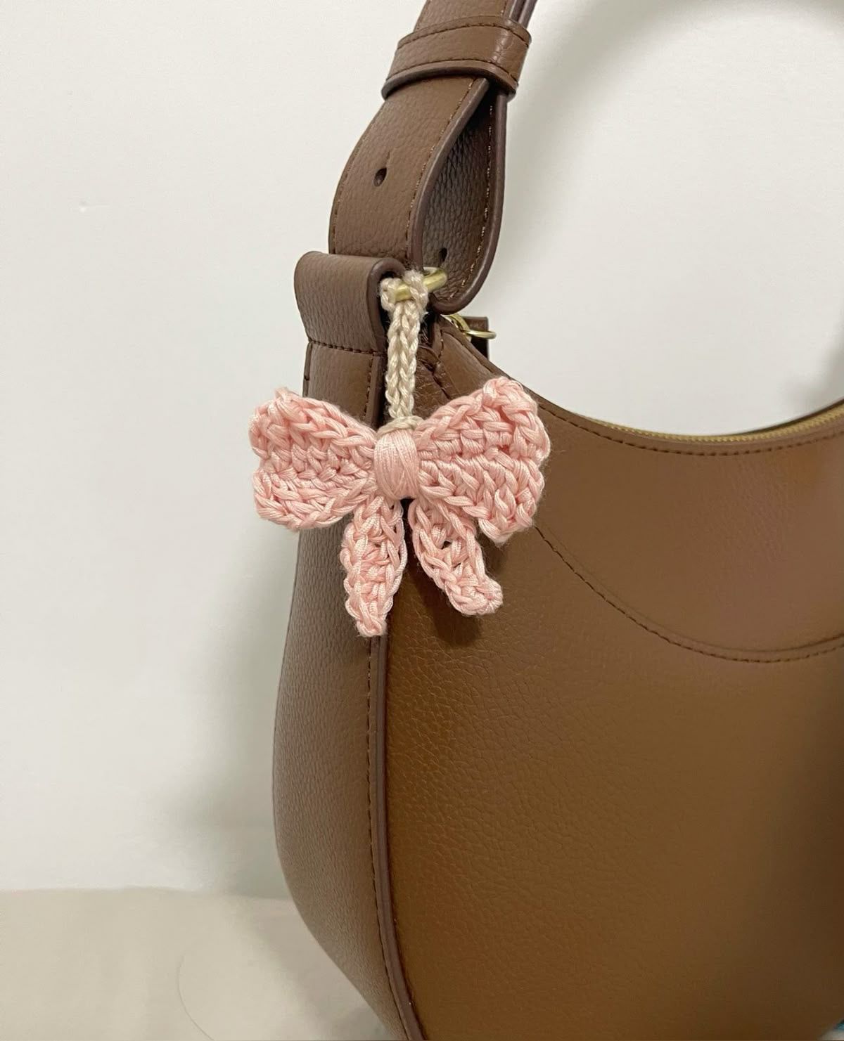 Brown handbag with a pink crocheted bow tied to the strap.