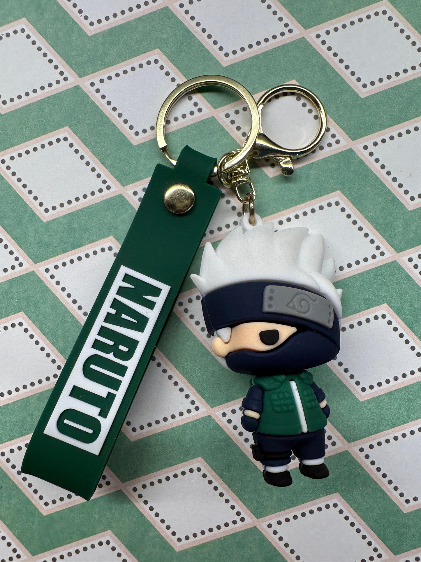 Keychain with Naruto character on a green strap against a patterned background
