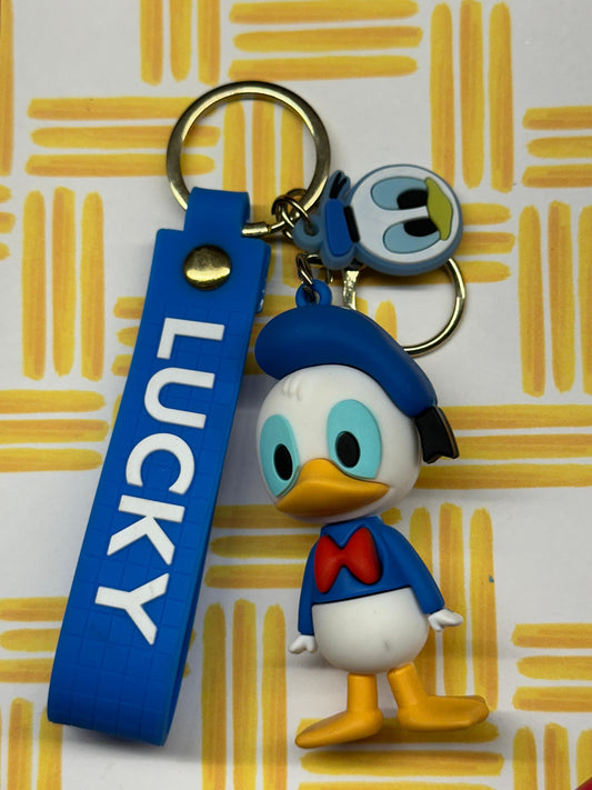 Donald Duck keychain with a blue “LUCKY” strap and a small face charm on a yellow patterned background.