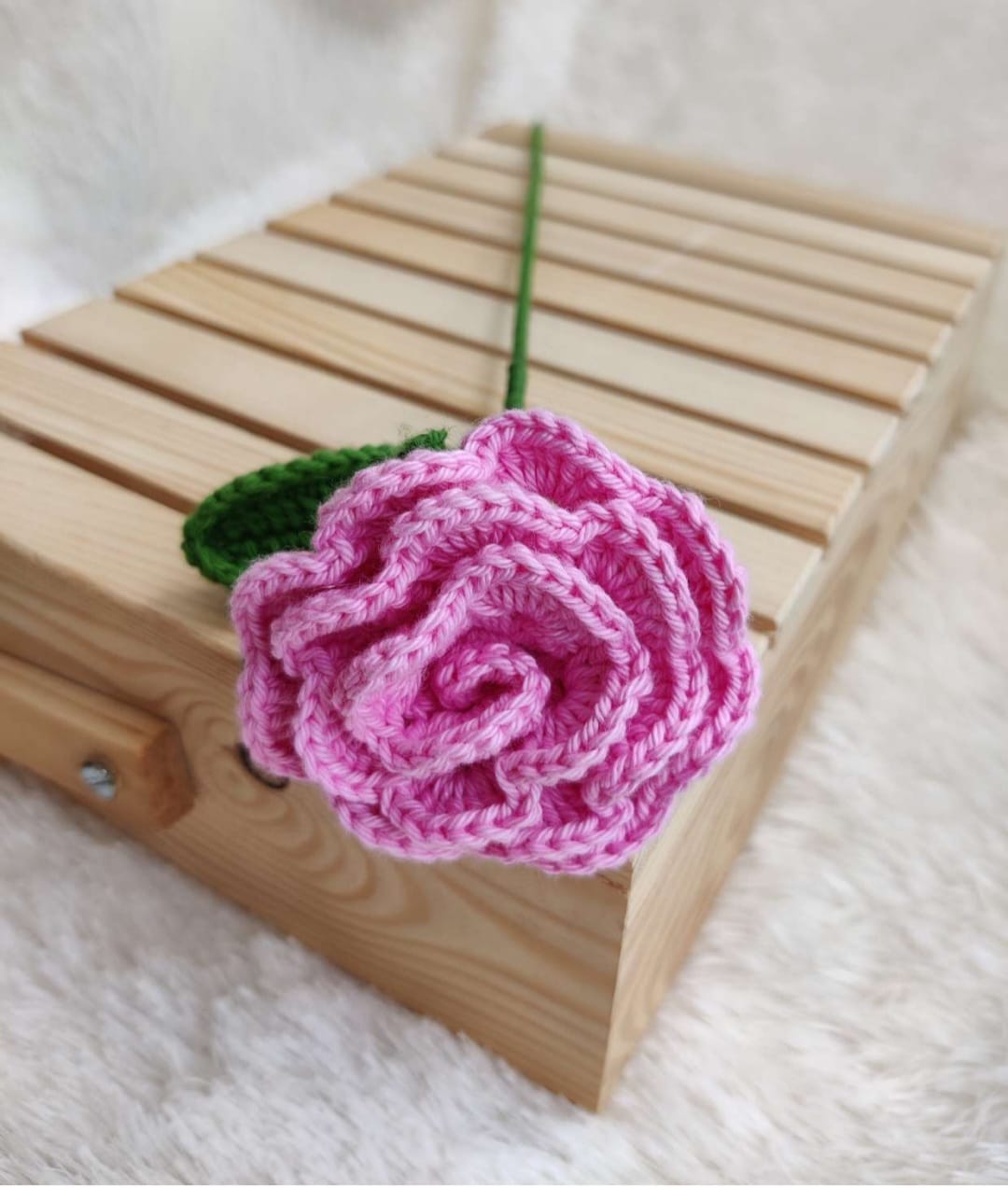Knitted pink rose on a wooden block with a white background
