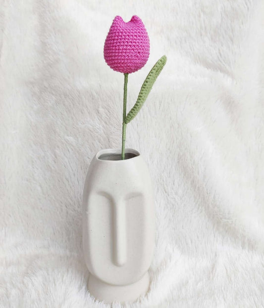 White face-shaped vase with a pink crocheted tulip on a white background